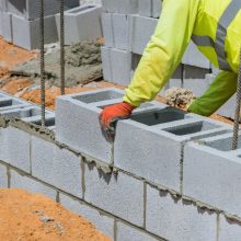 A mason is in the process of mounting a wall of aerated concrete blocks using masonry techniques on construction site